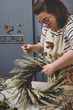 Woman making a winter wreath, adding dried grasses and seedheads and twigs with brown leaves