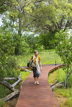 adult woman walking wooden path, tented camp, Botswana