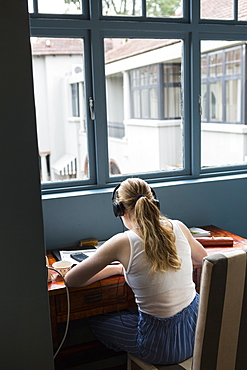 A thirteen year old girl wearing headphones doing homework seated in a quiet spot