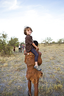 Five year old boy riding on shoulders of a San bushman