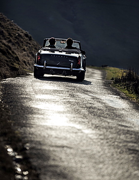 Rear view of two people in a convertible driving along a country road