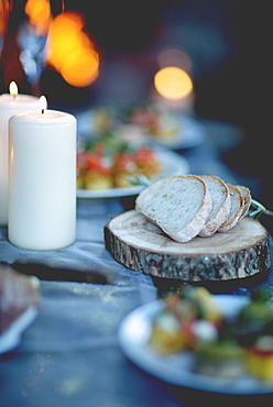 Close up of two lit candles and slices of bread on round wooden board