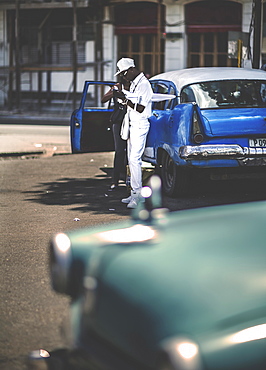 Two people standing by the open door of a classic 1950s car in a parking lot