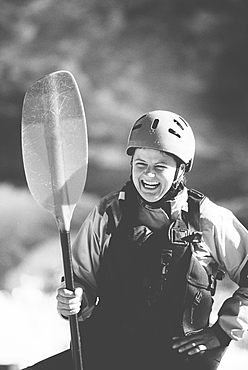 Female whitewater kayaker on a river bank holding a paddle