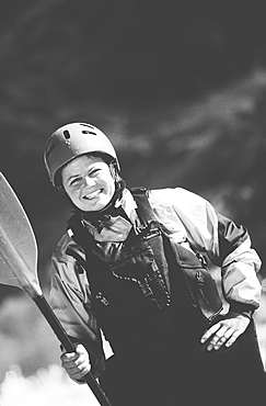 Female whitewater kayaker on a river bank holding a paddle