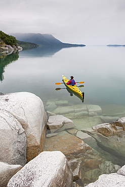 Female sea kayaker paddling pristine waters of Muir Inlet overcast sky in distance, Glacier Bay National Park, Alaska