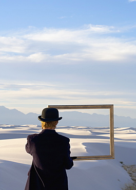 Man in a black coat and suit a bowler hat and umbrella in a white desert wilderness of white sand