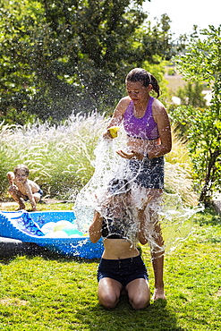 Two teenage girls wearing swimwear playing with water balloons in a garden, New Mexico, United States