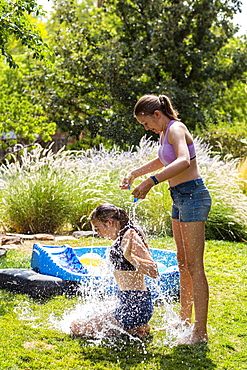 Two teenage girls wearing swimwear playing with water balloons in a garden, New Mexico, United States