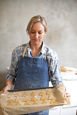 Blond woman wearing blue apron holding tray with Christmas Tree cookies