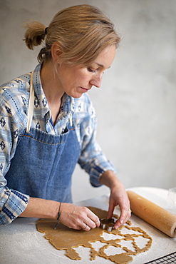 Blond woman wearing blue apron cutting out Christmas cookies