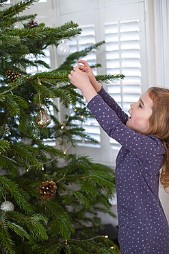 Young girl decorating Christmas tree with baubles