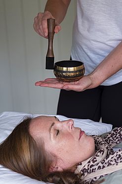 Woman on a couch, and a female therapist using Tibetan singing bowl, sound therapy