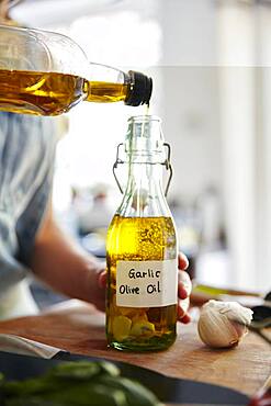 Woman pouring olive oil into bottle containing garlic