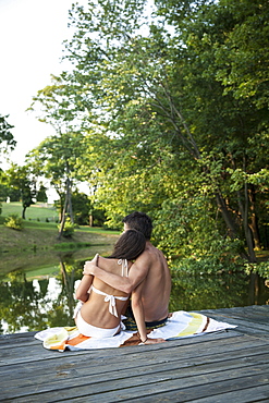 A young couple, boy and girl, sitting close together on a wooden jetty by a water pool, Maryland, USA