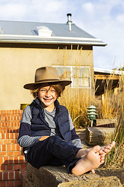 Portrait of young boy wearing fedora hat relaxing on his porch