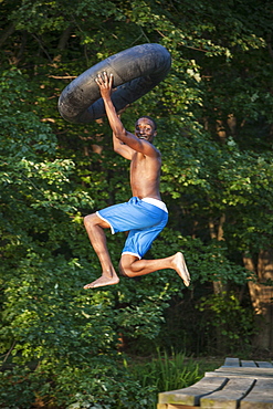 A young person, boy holding a swim float tyre over his head and leaping into the water from the jetty, Maryland, USA