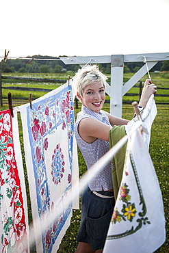 A young girl, teenager, hanging out the washing, pegging patterns fabric sheets to a washing line, Maryland, USA