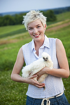 A young girl, teenager, holding a chicken with white feathers in her arms, Maryland, USA