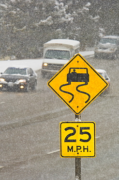 Traffic driving on snowy road with road sign warning of skid danger