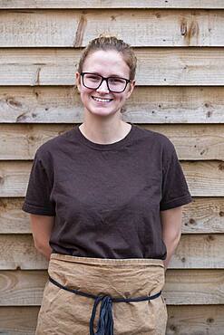 Portrait of female barista with blond hair and glasses, leaning against wall on a break