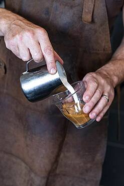 Close up of barista wearing brown apron pouring cafe latte.