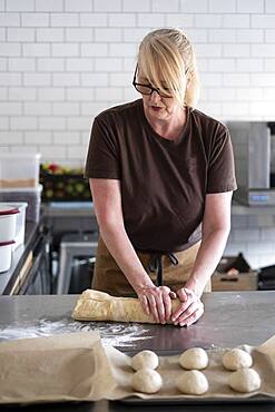 Woman in brown apron standing in a cafe kitchen, mixing baking danish pastry dough