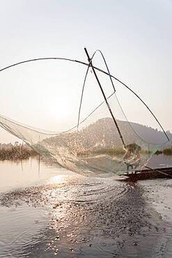 Fisherman on his boat moving arched swing nets above the water at  Loktak Lake