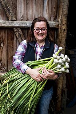 Smiling woman holding bunch of freshly picked garlic, Oxfordshire, United Kingdom