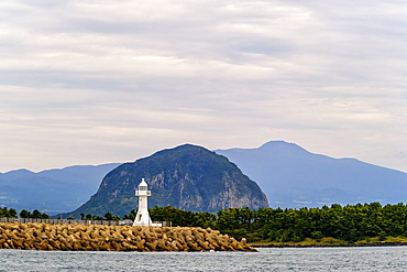 One of Jeju Island's many lighthouses stands against Mount Sanbangsan and Mount Hallasan, a shield volcano, Jeju Island, South Korea, Asia