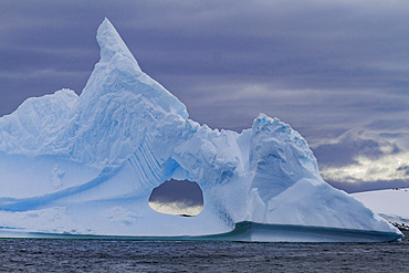 Unusual window formation in iceberg showing Booth Island in the background on the western side of the Antarctic Peninsula.