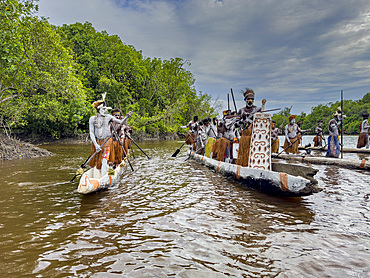 Male paddlers from the village of Uwus perform in a ritualistic greeting ceremony, Asmat Region, Papua, Indonesia.