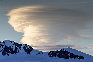 Shorefast ice and snow covered mountains with a lenticular cloud build up in Wilhamena Bay, Antarctica, Polar Regions