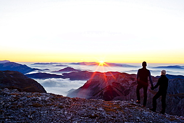 Two hikers at summit of Hochschwab mountain at sunrise, Hochschwab, Styria, Austria