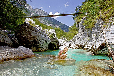 Young woman sitting in the river Soca, Alpe-Adria-Trail, Tolmin, Slovenia