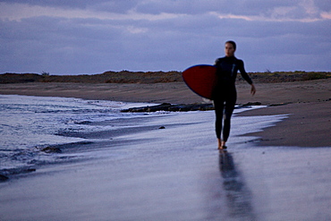 Female surfer walking along sandy beach, Praia, Santiago, Cape Verde