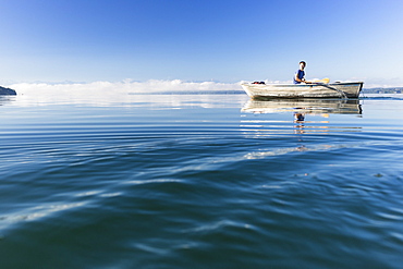 Man in a rowboat on lake Starnberg, the Alps and mount Zugspitze in early morning fog, Berg, Upper Bavaria, Germany