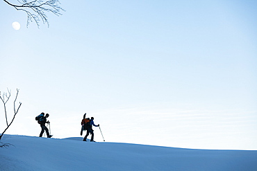 Backcountry snowboarder and snowshoe hikers at dusk in the Tennengebirge mountains, Bischofsmuetze in the background, Salzburg, Austria