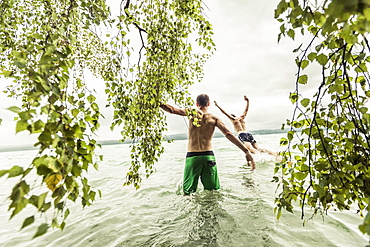 two young men going swimming in Lake Starnberg near a birch tree, Berg, Upper Bavaria, Germany