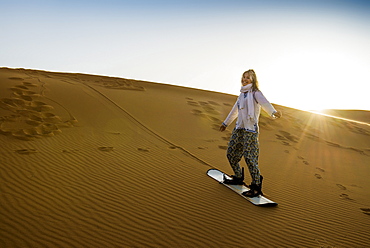 young woman with snowboard, sand dunes near Merzouga, Erg Chebbi, Sahara Desert, Morocco, Africa