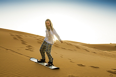 young woman with snowboard, sand dunes near Merzouga, Erg Chebbi, Sahara Desert, Morocco, Africa