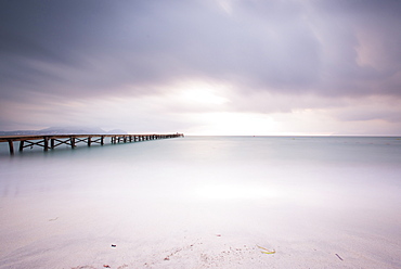 Long exposure of a wooden pier on Playa de Muro beach in the morning mood. The sky is overcast and fog lies over the Bay of Alcudia. Alcudia, Mallorca, Balearic Islands, Spain