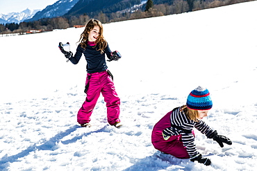 girl throwing a snowball towards a boy during a snowball fight in winter, Pfronten, Allgaeu, Bavaria, Germany