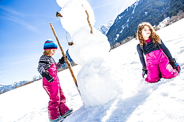 girl and boy building a snowman in winter, Pfronten, Allgaeu, Bavaria, Germany