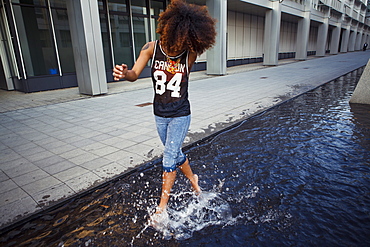 Sportive, young afro-american woman running through a water fountain in urban scenery, Munich, Bavaria, Germany