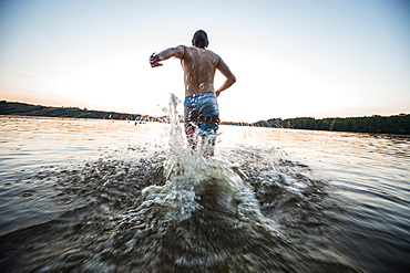 Young man running into the water of a lake, Freilassing, Bavaria, Germany