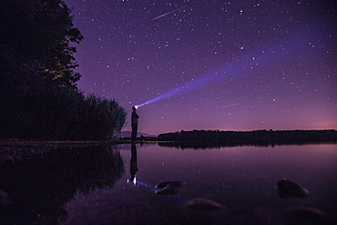 Young man standing at a lake and looking towards the stars, Freilassing, Bavaria, Germany