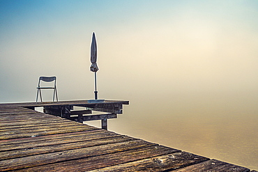 Jetty with folded parasols at misty sunrise on Lake Starnberg, Seeshaupt, Bavaria, Germany