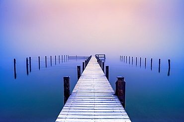 Snow-covered jetty in marina at misty sunrise on Lake Starnberg, Seeshaupt, Bavaria, Germany