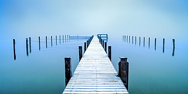 Snow-covered jetty in marina at misty sunrise on Lake Starnberg, Seeshaupt, Bavaria, Germany